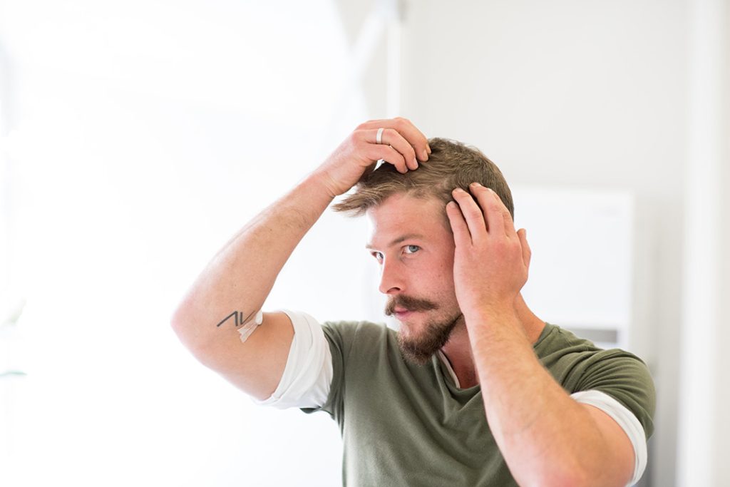 a man touches his hair and looks in the mirror